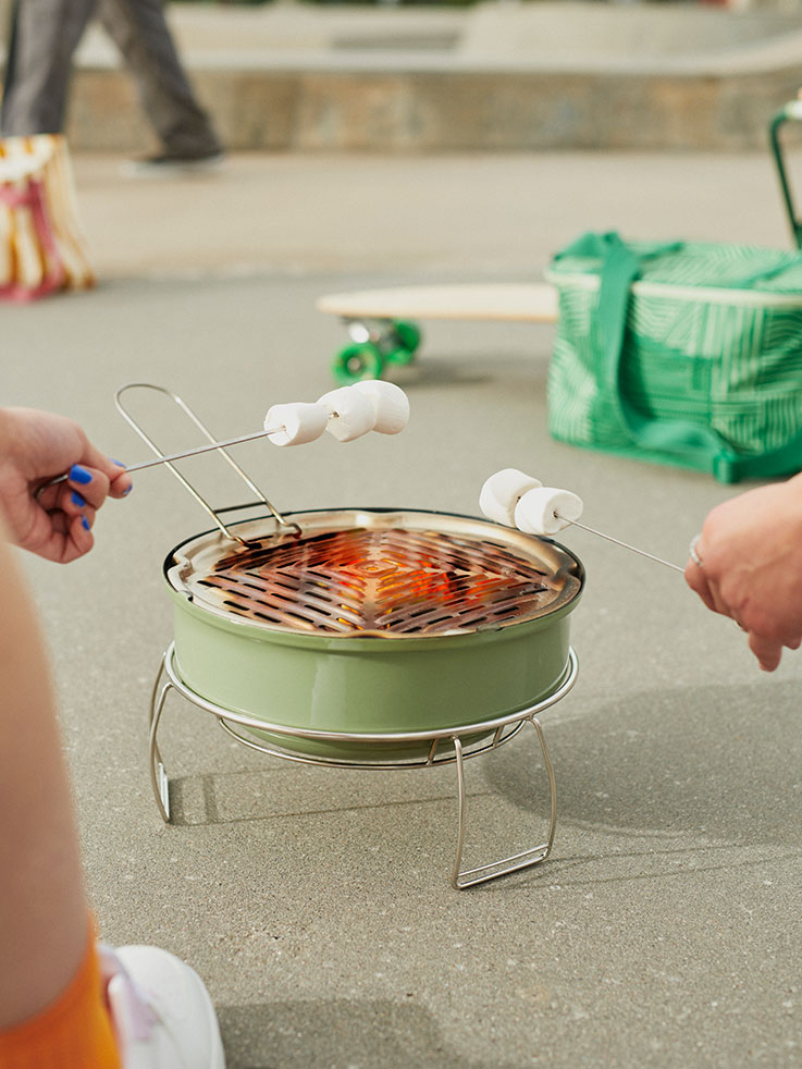 Hands roasting marshmallows on a mini green grill. Fun, sweet outdoor atmosphere.