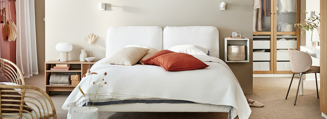 Bedroom with white headboard bed, earth-toned cushions and wardrobe with ribbed glass doors.