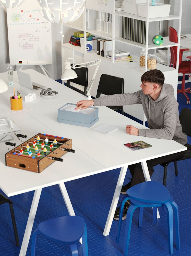 Wide white meeting tables surrounded by blue benches in a creative and modern environment there is a person interacting with the creative items on the table.