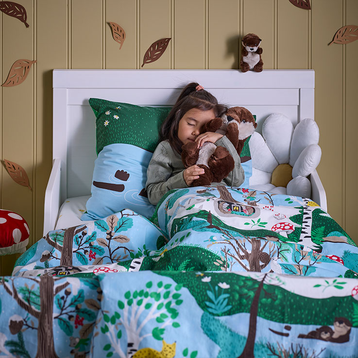 Girl sleeping with plush toy on blue nature-patterned bedding. Childish and cozy atmosphere.