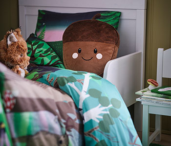 Kids' bed with smiling acorn pillow, plush otter, forest bedding. Cozy atmosphere.