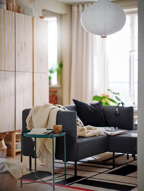 Salón con un sofá con una manta extendida, una mesa y una silla, decorado de manera moderna.
