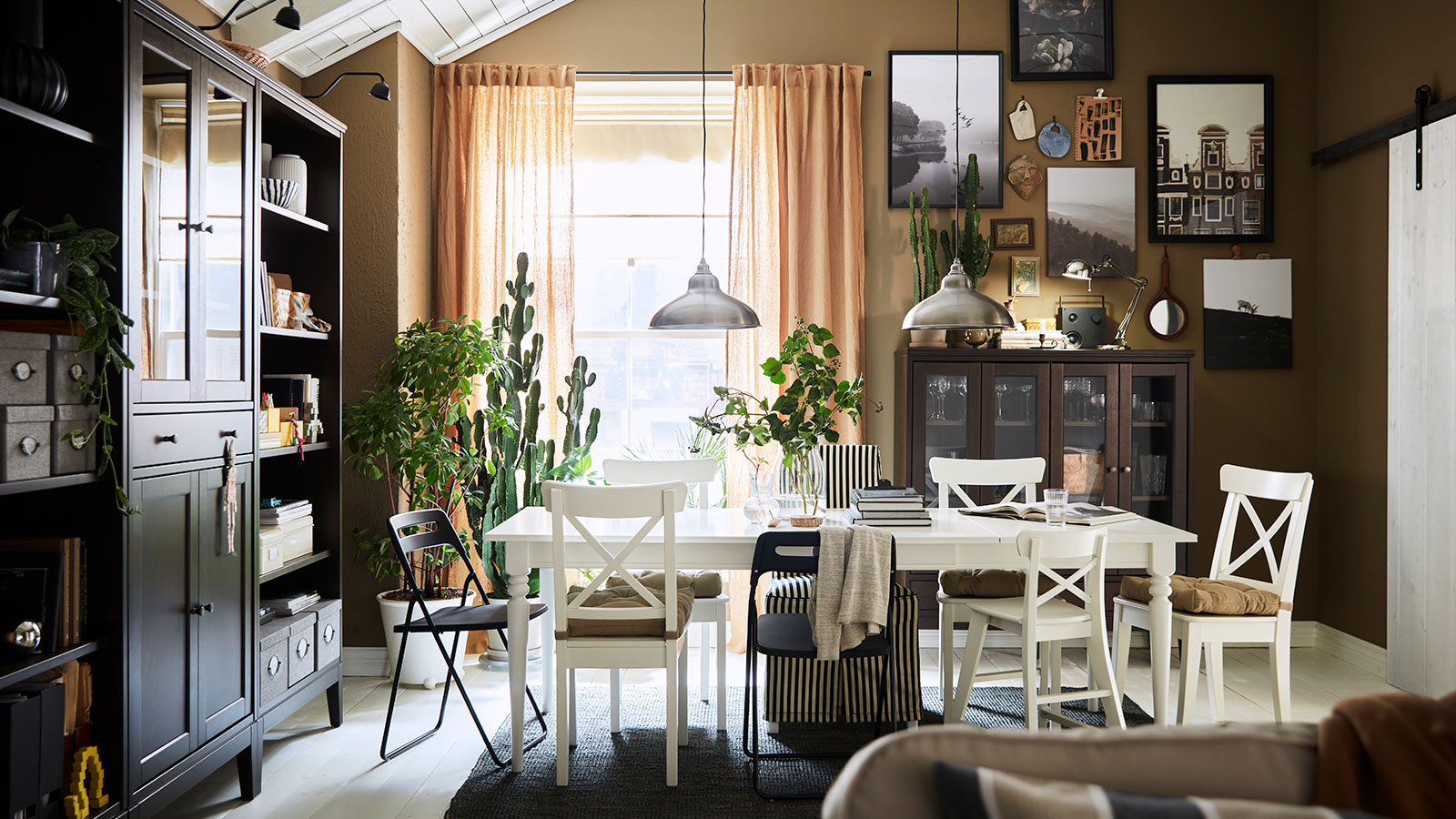 Traditional style dining room with vintage touches, white table, chairs with cushions, a large window with beige curtains, on the wall to the right a bookshelf and display case, in the background a showcase.
