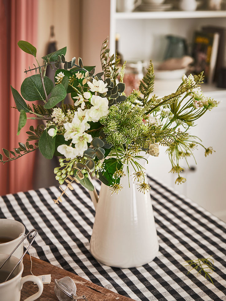 White vase-shaped vase on a traditional style table with a black and white checkered tablecloth.