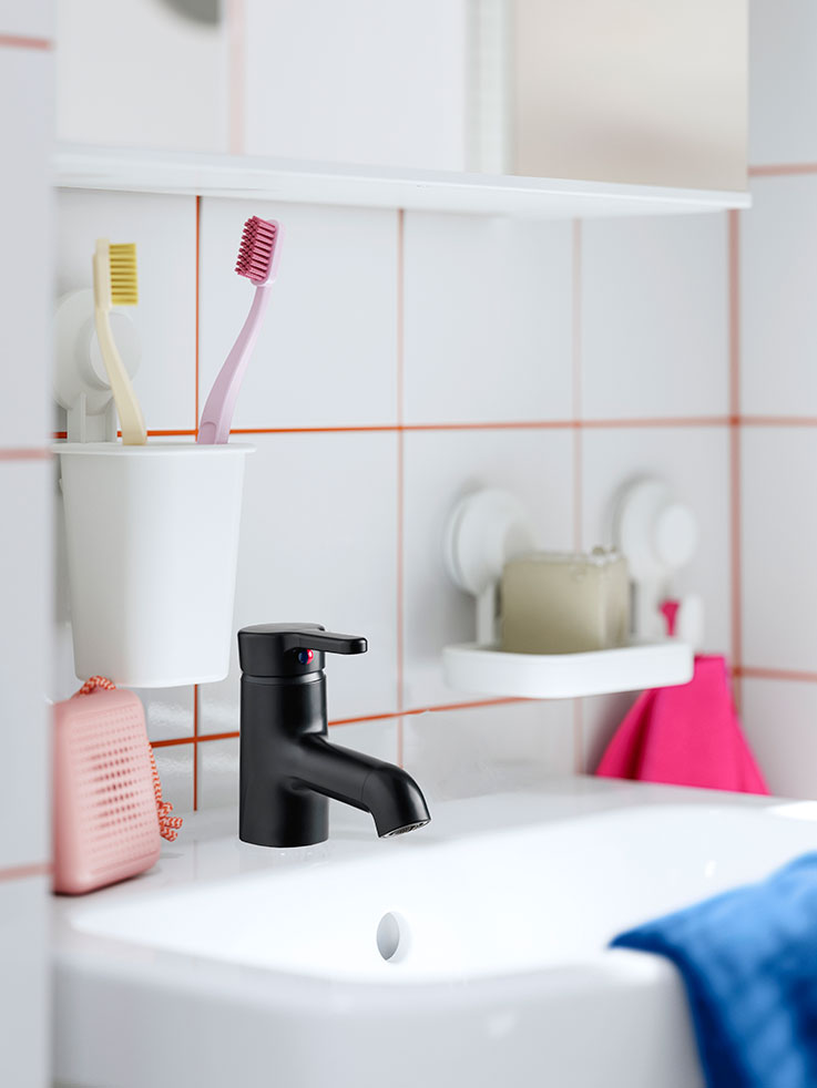  Black faucet on white sink, colorful toothbrushes. Clean and modern bathroom.