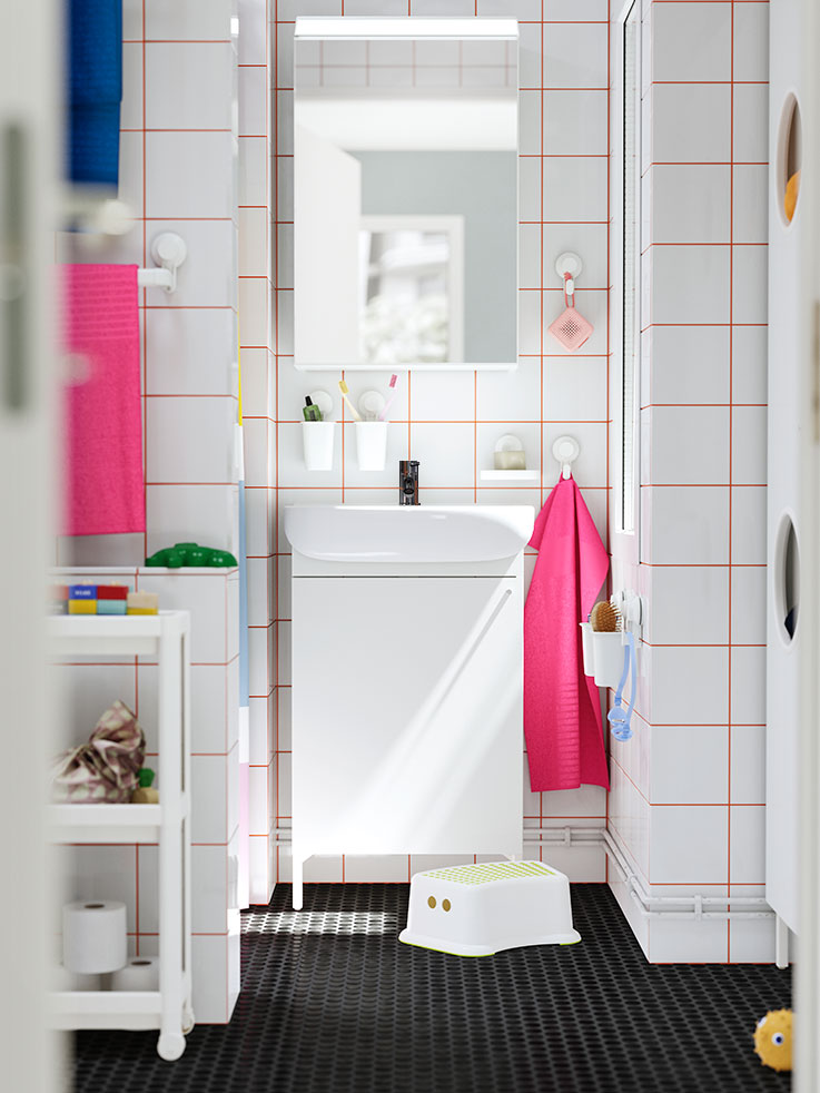 White bathroom with orange tiled grout. Pink towels, white step stool. Clean and functional atmosphere.