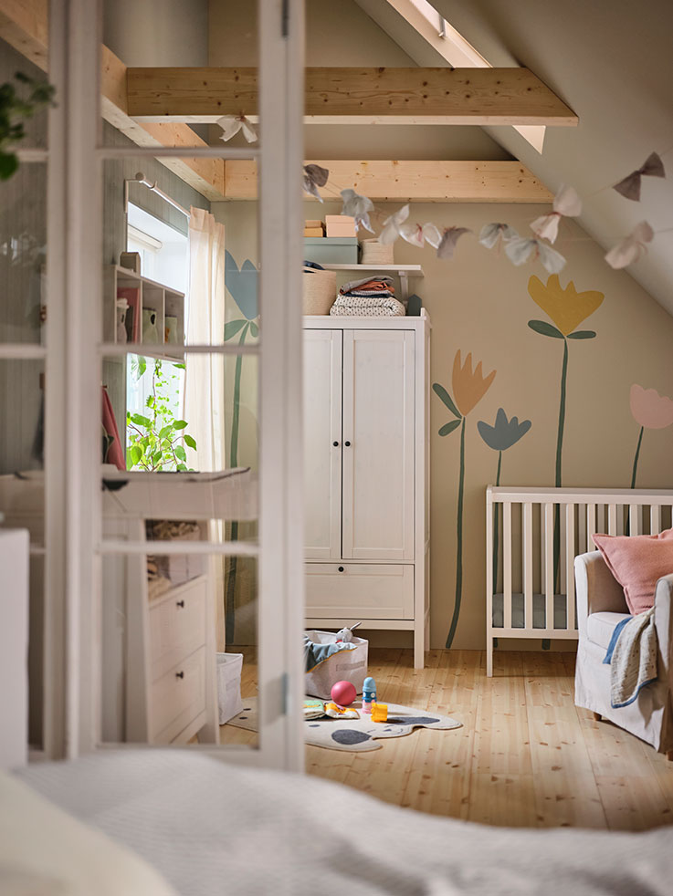   A baby's room, a changing table in front of a window, a modular shelf, a closet next to a crib and toys on the floor next to a curtain.