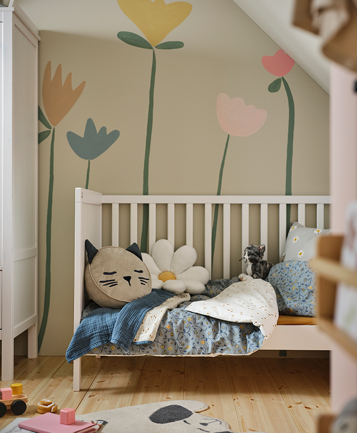A baby room with a SUNDVIK crib, a GULDVÄVARE quilt on top, and a BARNDRÖM cushion, with a DRÖMSLOTT rug on the floor.