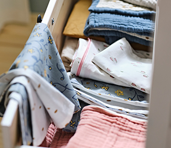 An open drawer with GULDVÄVARE crib sheets, a 3-piece GULDVÄVARE crib set, and a GULDVÄVARE duvet set.