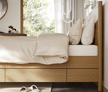 Wooden bed with under-bed storage, beige bedding, and natural light coming through the window.