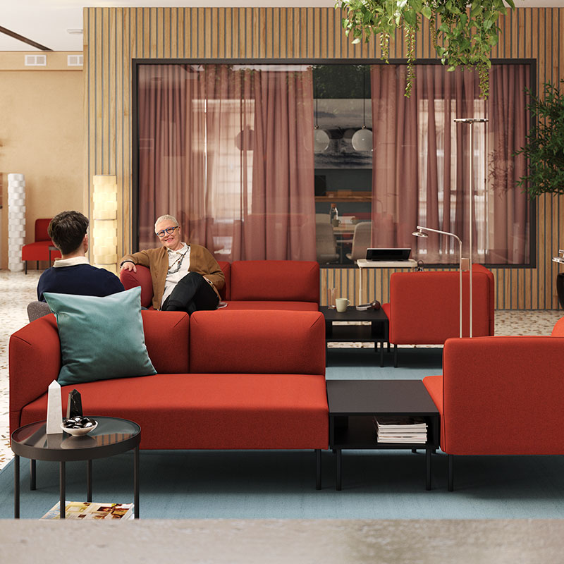 Modern lounge with red sofas, people chatting, and cozy decor.