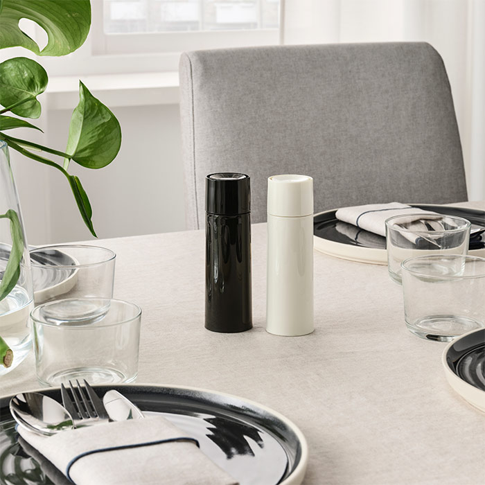 Dining table set with black/white grinders, dark plates, clear glasses, silverware, and a green plant. Grey chair.