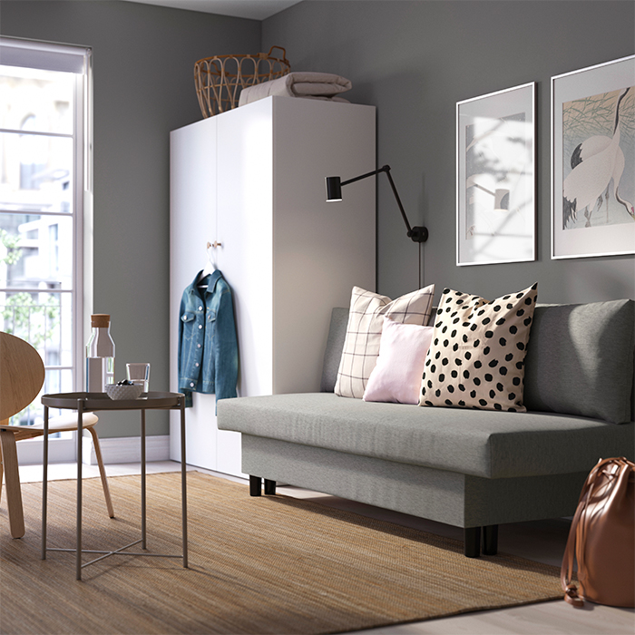 A cozy, modern living room with a gray sofa, patterned pillows, and natural light streaming through a window.