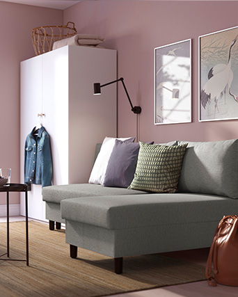 A cozy living room corner with a gray sofa, decorative pillows, wall art, and a white wardrobe against a pink wall.