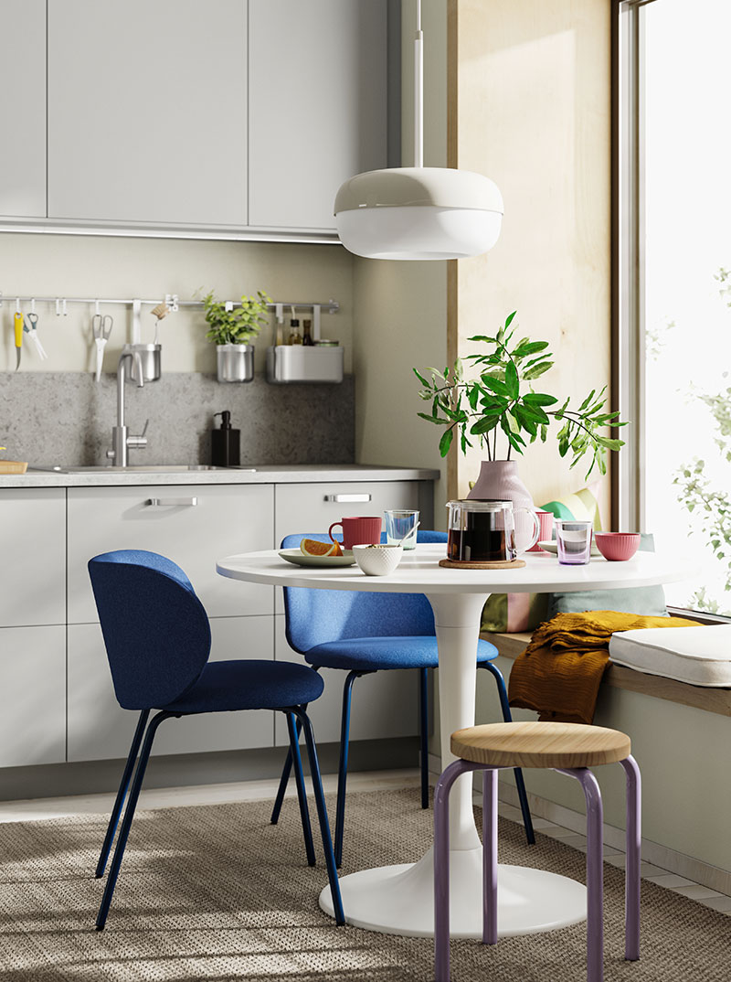 Modern gray and white kitchen, round table with blue chairs and purple stool. Bright atmosphere.