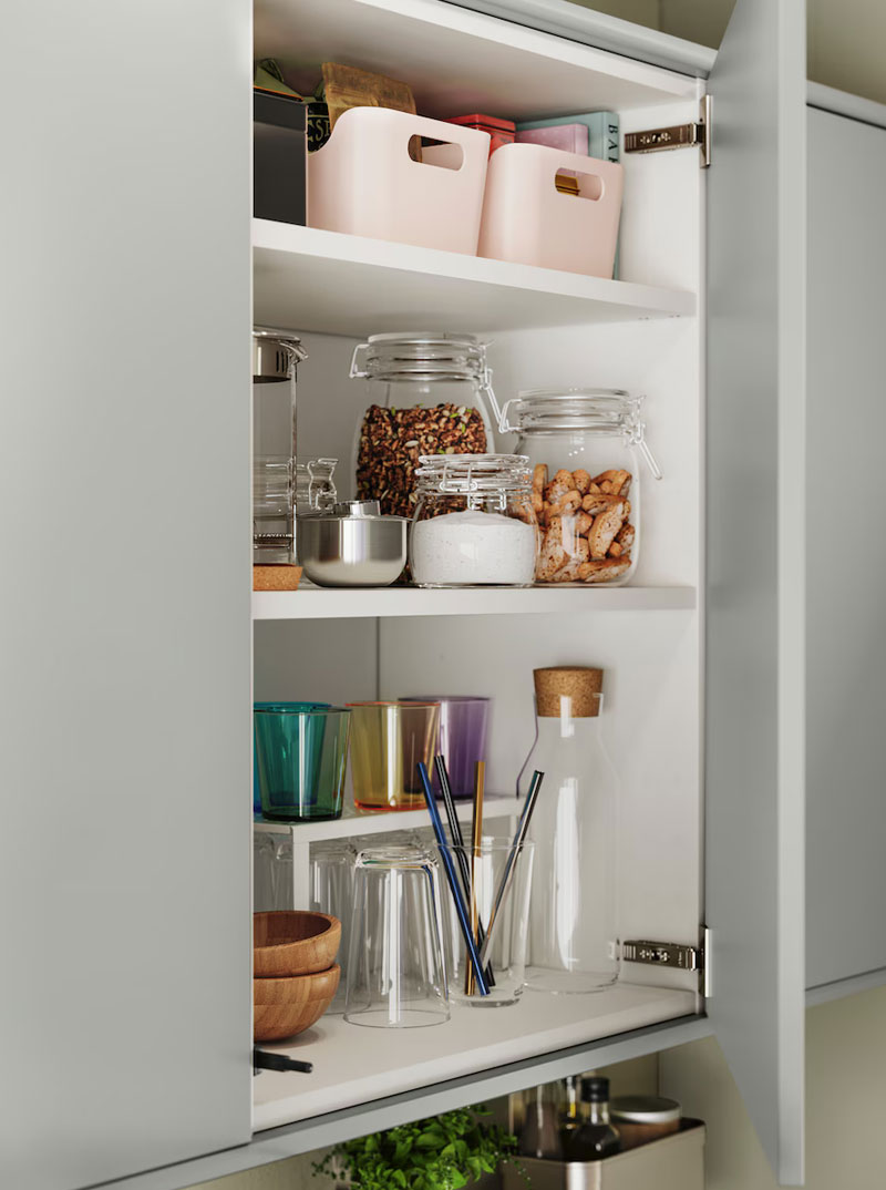 Open kitchen cabinet with shelves full of jars, colorful glasses, and baskets. Organized.