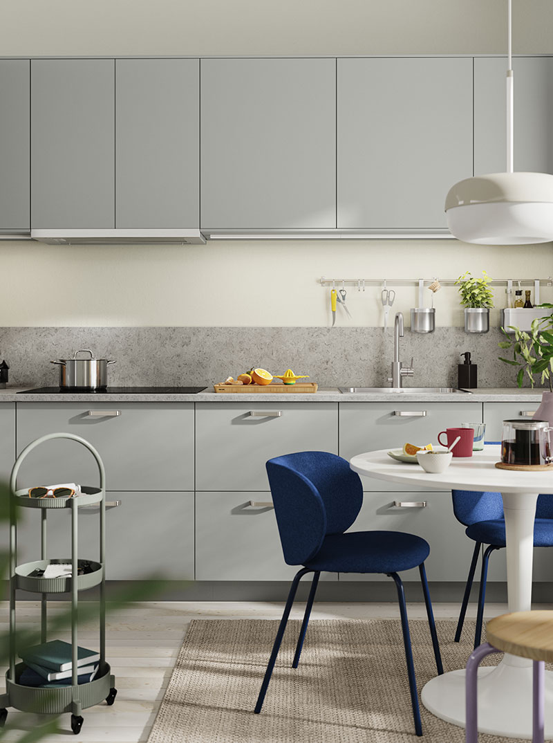Modern kitchen with gray cabinets, white round table, and blue velvet chairs. Bright.