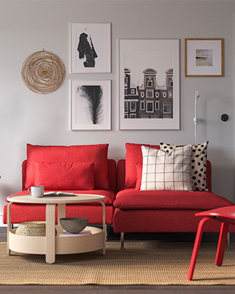Modern red sofa with striped and dotted cushions, round wooden coffee table in a modern style, and four framed photo prints on the wall.