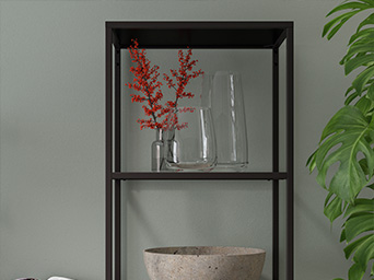 Un estante de metal oscuro muestra jarrones de vidrio transparente, uno con flores rojas vibrantes, y un cuenco beige texturizado, junto a una planta verde.