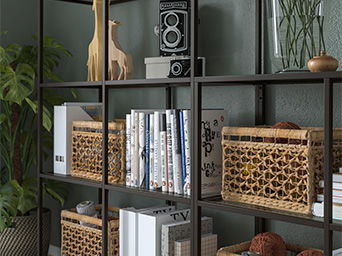 Estantería de metal oscuro con libros, cestas de mimbre, jirafas decorativas, cámara antigua y planta, creando una exhibición acogedora.