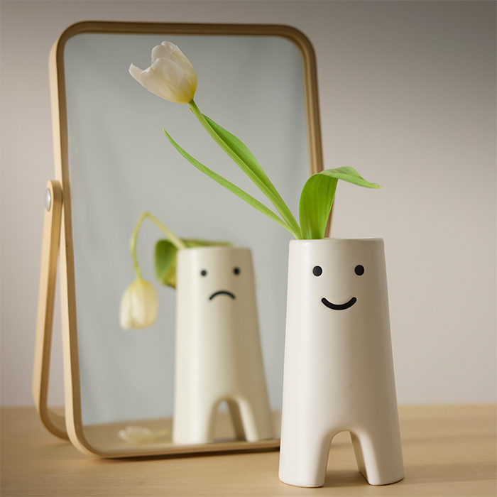 White vase with a smiling face reflected in a small mirror