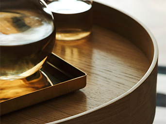 A close-up of a wooden tray holding a glass decanter and cup with amber liquid, reflecting warm light.