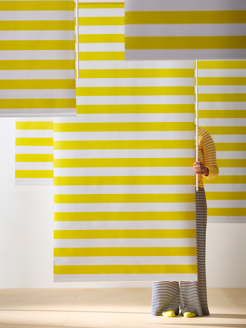 A person standing in front of a wall decorated with yellow and white striped blinds.