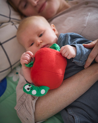 Baby holding a red apple-shaped plush toy with a little green worm peeking out