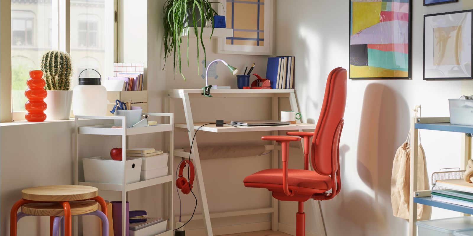 Espacio de estudio luminoso y moderno con escritorio blanco, silla ergonómica roja y decoración colorida, ideal para trabajar o estudiar en casa.