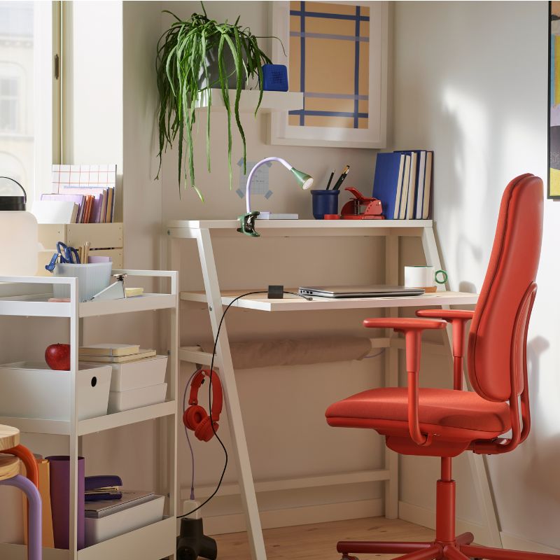 Espacio de estudio luminoso y moderno con escritorio blanco, silla ergonómica roja y decoración colorida, ideal para trabajar o estudiar en casa.