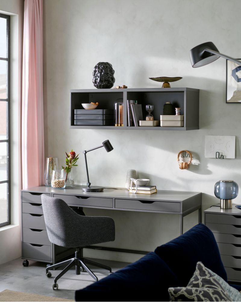 Oficina en casa con escritorio gris, silla giratoria y estantería de pared, ideal para un espacio de trabajo moderno y organizado.