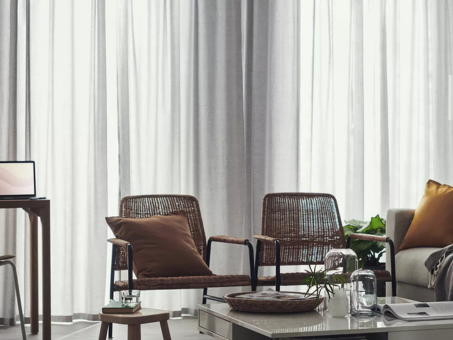 Salón moderno con sillones de ratán, cortinas traslúcidas y mesa de centro decorada.
