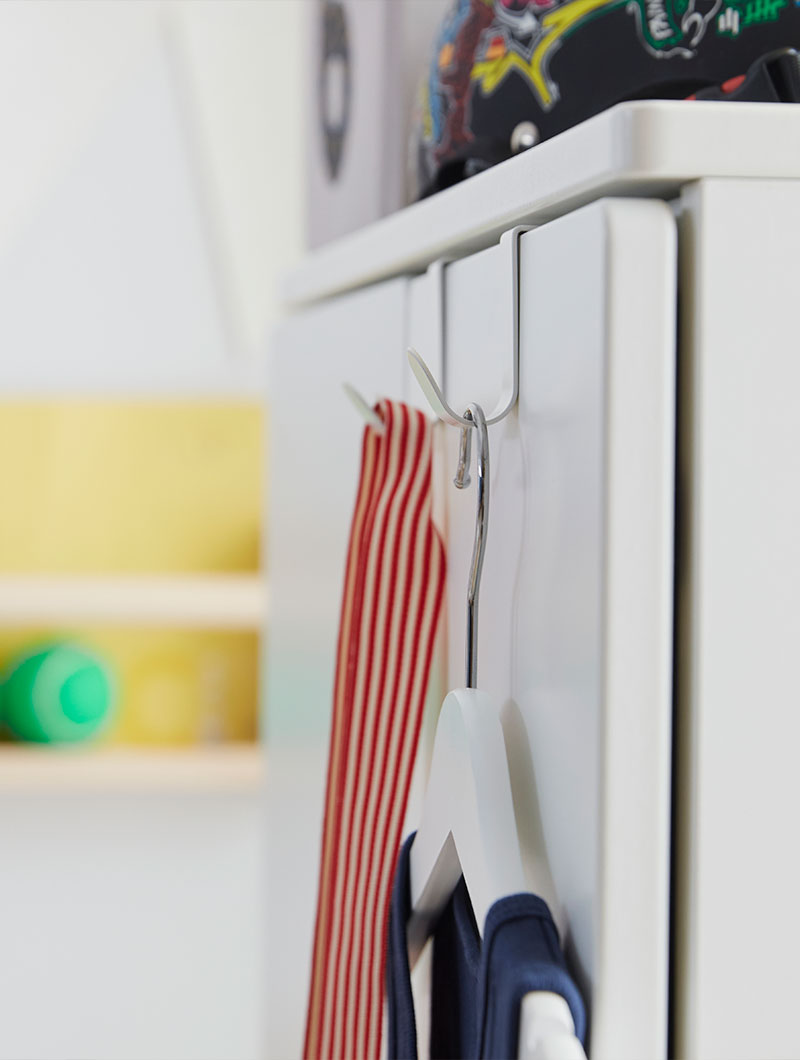 The white LÄTTHET hooks used on the exterior of SMÅSTAD storage for hanging clothes in a colourful children’s room