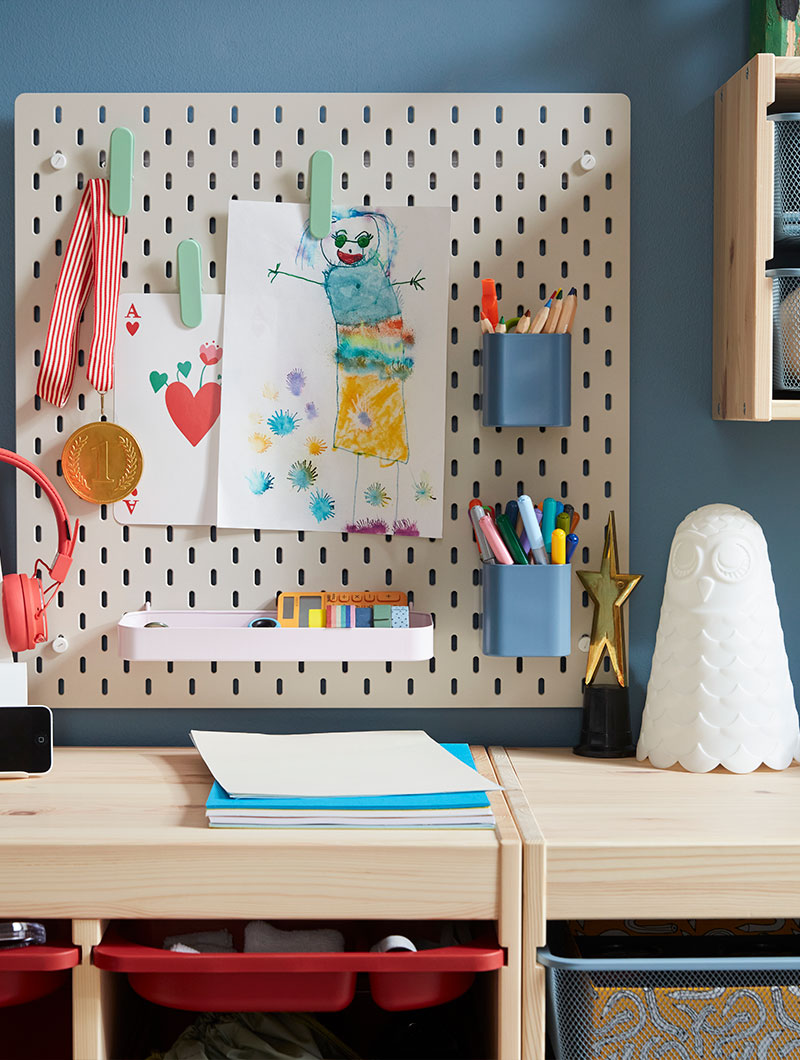 A beige SKÅDIS pegboard with colourful accessories such as containers, clips and a shelf, placed on a blue wall above storage