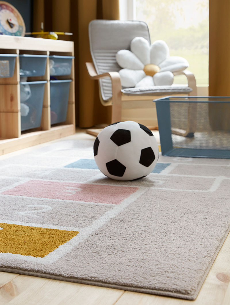 The soft STÄPPSVARV rug with a hopscotch pattern placed in a kid’s room with a textile football by TROFAST storage units