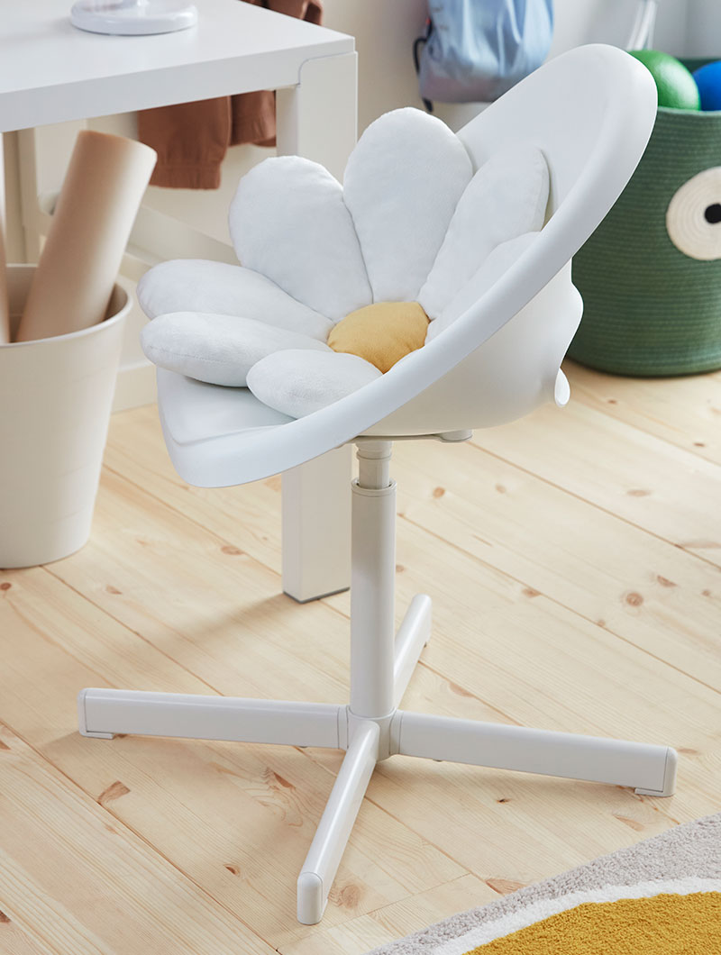 A daisy cushion is placed in a POÄNG children’s armchair in beige standing by a window in a children’s room with storage