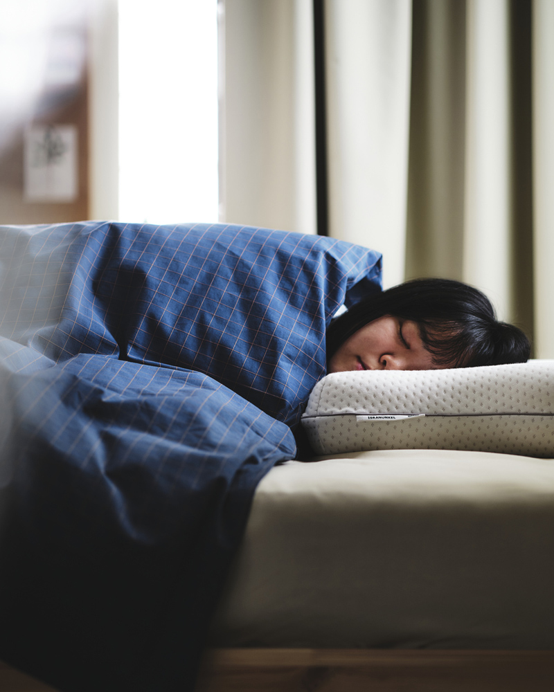 A person asleep under blue/brown DOFTAKLEJA bed linen with their head on an ISRANUNKEL multi-position ergonomic pillow.