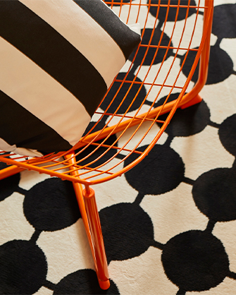 Orange metal chair on a black and white rug with a circular design. A vibrant touch that highlights your space.