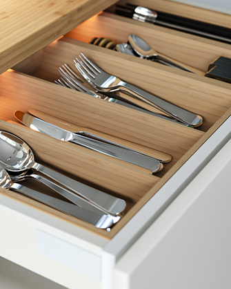 Cajón de cocina abierto con organizadores de bambú para cubiertos, mostrando tenedores, cuchillos y cucharas, con iluminación interna para visibilidad.