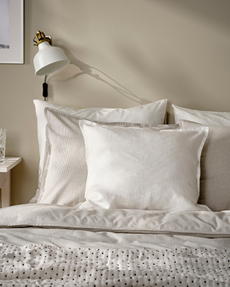 Rincón de una habitación con estanterías flotantes blancas y cortinas claras. Las estanterías sostienen jarrones con plantas, libros y un teléfono, organizando el espacio vertical.