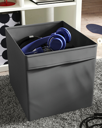 Dark gray storage box containing blue headphones. Functional solution for organizing electronics and cables in living rooms or playrooms.