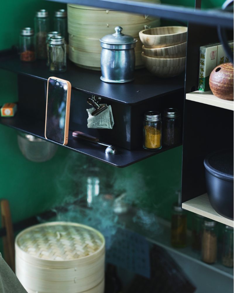 Steam is rising in a kitchenette and into a VIGGBO wall mounted extractor hood, with small bowls and jars sitting on it. 