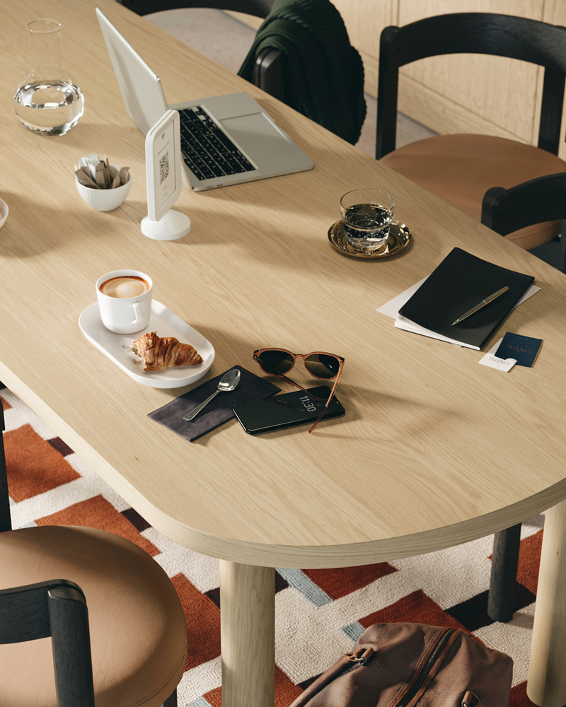 A close-up of a STOCKHOLM 2025 table in oak veneer with 6 dark brown chairs, arranged with coffee and pastries.