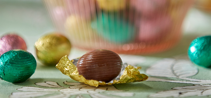 Un primer plano de un huevo de chocolate con leche VÅRKÄNSLA, sobre un mantel verde SMÖRFISK con estampado floral.