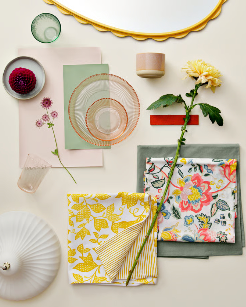 A folded yellow and white FJUNKLOCKA cushion cover placed among other items, flowers, and textiles in a stylish arrangement.