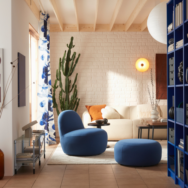 A living room with a Gunnared dark blue LILLESÄTER swivel easy chair in soft fabric beside an off-white sofa and green plants.