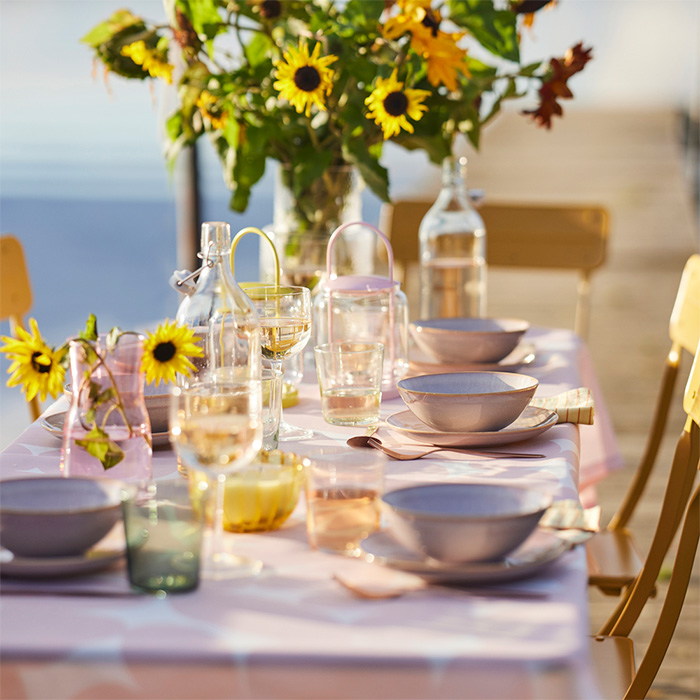 Outdoor summer table decorated with yellow flowers, pastel tableware, and glassware under a warm and inviting golden light.