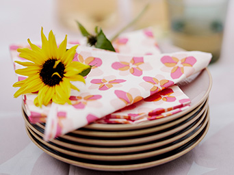 Stack of plates with floral napkins and a sunflower under soft lighting.