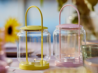 Two glass lanterns, one yellow and one pink, with lit candles on a cozy table.