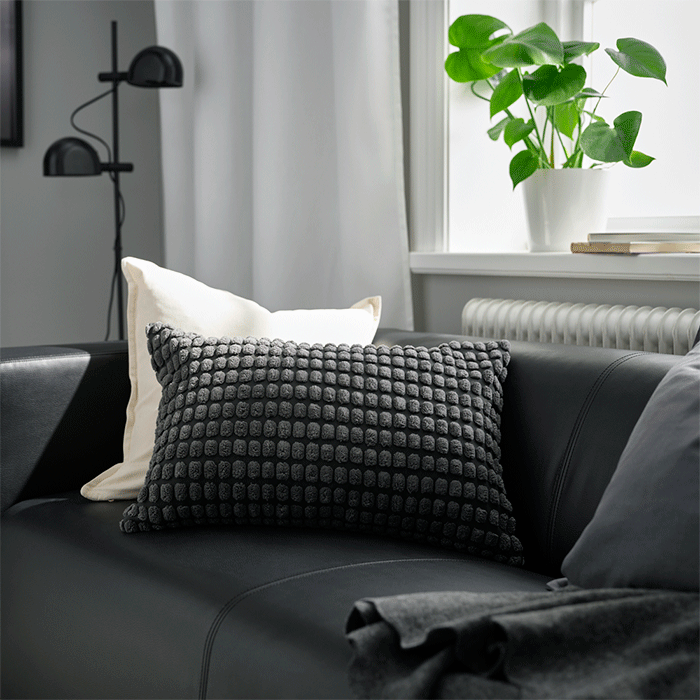 Cojines con textura en gris oscuro y blanco sobre un sofá de piel negra en un salón luminoso.
